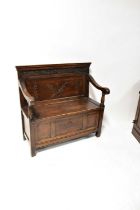 A reproduction small settle with carved decoration and lift-up seat enclosing a storage section,