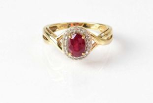 A 9ct yellow gold cluster ring set with central red stone in a surround of diamonds, in claw