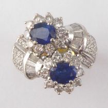 A vintage Art Deco style sapphire and diamond cross-over ring, with two claw set oval sapphires in a