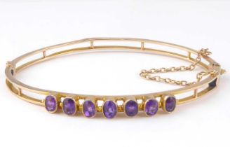 A 9ct gold amethyst hinged bracelet with seven bezel set cut amethysts in a double-track frame, with