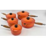 LE CREUSET; a set of five orange enamel cast iron lidded saucepans.