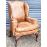 A Georgian style leather upholstered wing armchair on shell capped cabriole supports with ball and