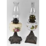 Two Victorian oil lamps with decorative cast iron bases, one with floral decorated ceramic bowl