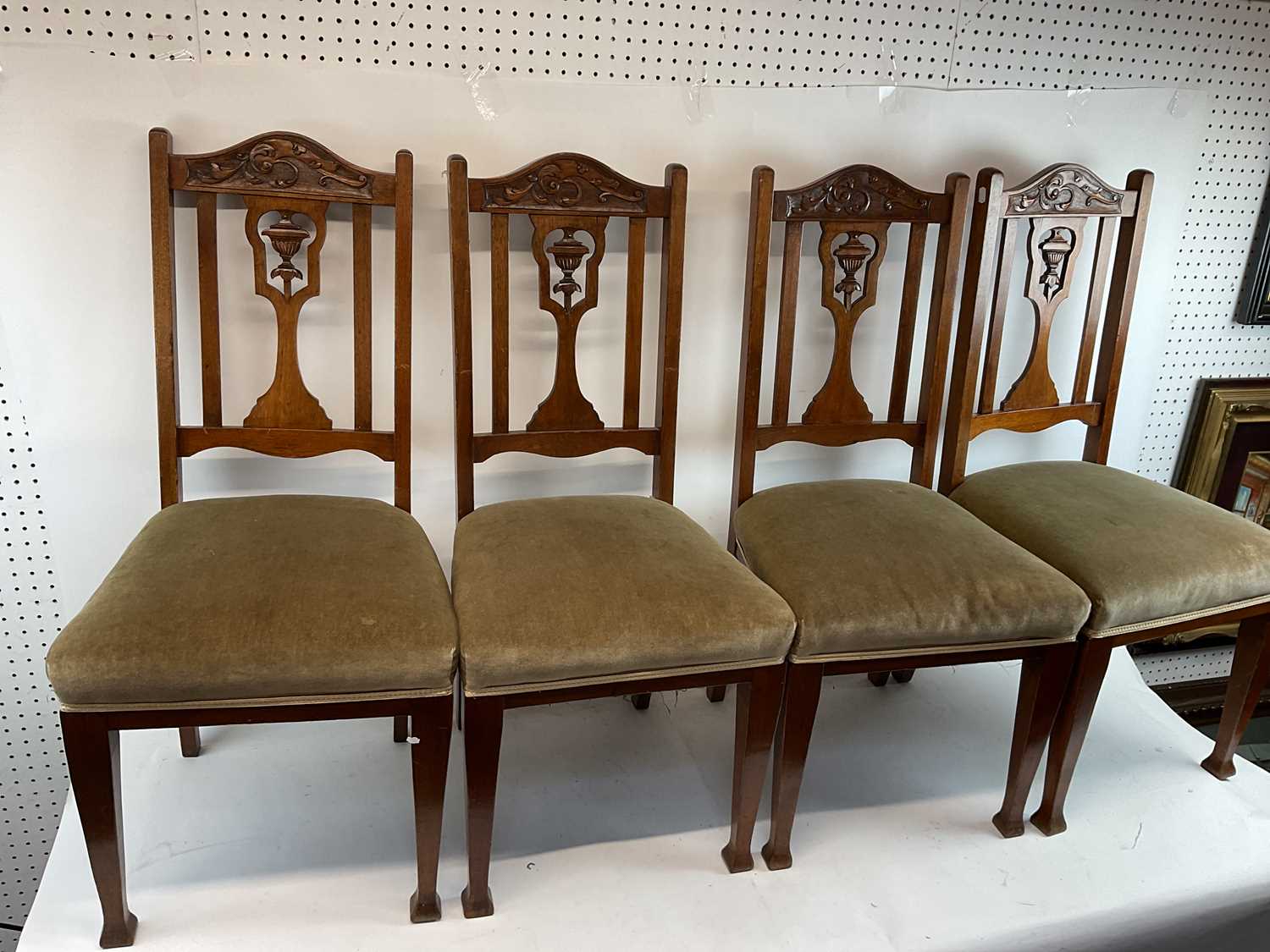 A set of four carved oak upholstered dining chairs with central urn decoration on pad feet.
