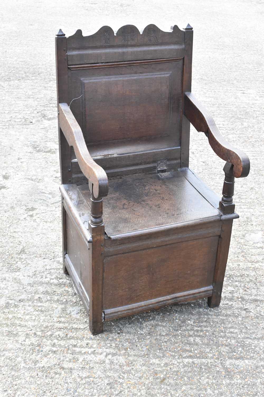 An 18th/19th century oak wainscot type chair with panel back, open arms and hinged seat.Condition