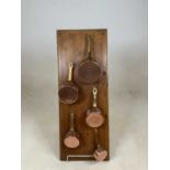 Five small graduated copper and brass pans mounted on a pine board, length of largest pan 21cm.