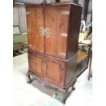 A 1950s walnut cocktail cabinet, the twin upper doors with elaborate brass strap detail enclosing