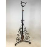 A wrought iron adjustable standard lamp with elaborate scroll detail to the tripartite base.