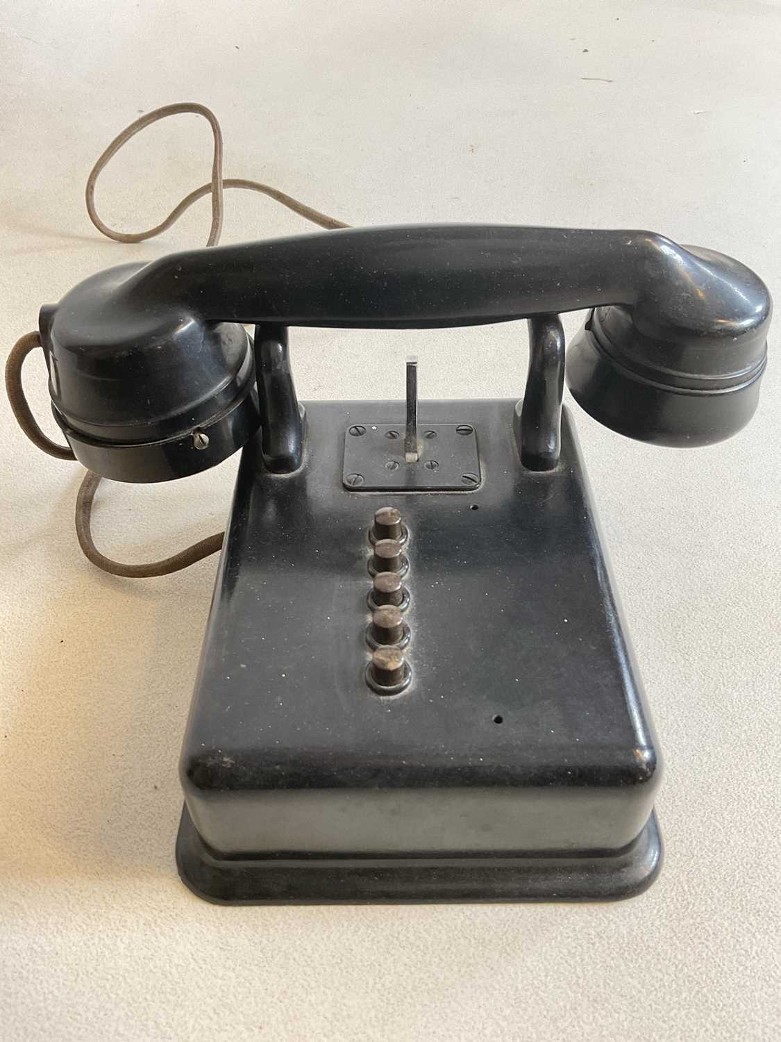 A vintage black bodied wall mounted telephone with five buttons and no dial.