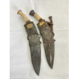 A pair of ornately decorated kukri knives with elaborate applied detail to the leather scabbards and