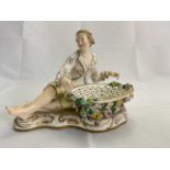 A late 19th century Continental porcelain figure of a young gentleman reclining beside a floral