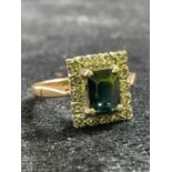 An 18ct yellow gold emerald and diamond ring with emerald cut emerald within a border of small