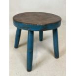 A rustic circular low stool with blue painted detail and raised on four legs.