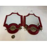 A pair of shaped wall mirrors with the glass plate on a red velvet ground and each set with twin