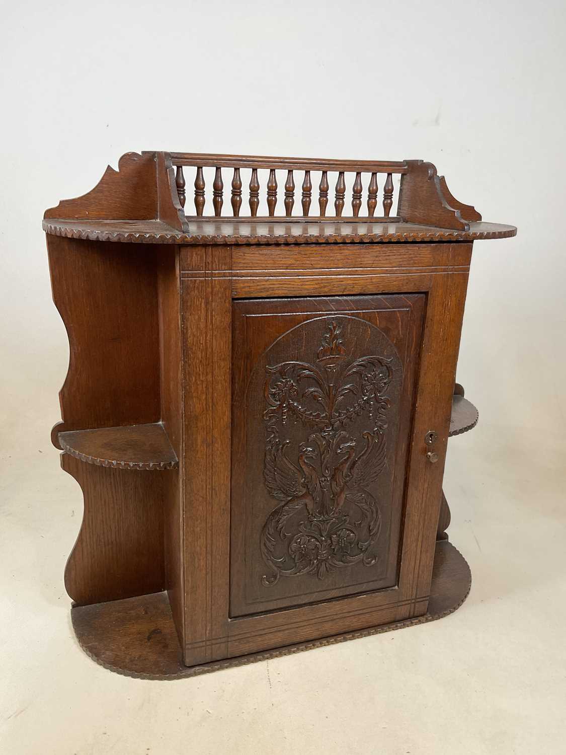 A circa 1900 oak hanging cabinet with spindle gallery above intricately carved hinged door enclosing