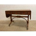 A Regency style sofa table with three frieze drawers raised on shaped end supports to brass paw feet