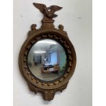 A French Regency style gilded circular convex wall mirror with eagle surmount and ebonised slip,