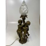 An early 20th century French bronze table lamp modelled as two putti supporting a frosted glass