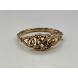 An Edwardian 9ct yellow gold hinged bangle with pierced knot upper platform with textured detail,