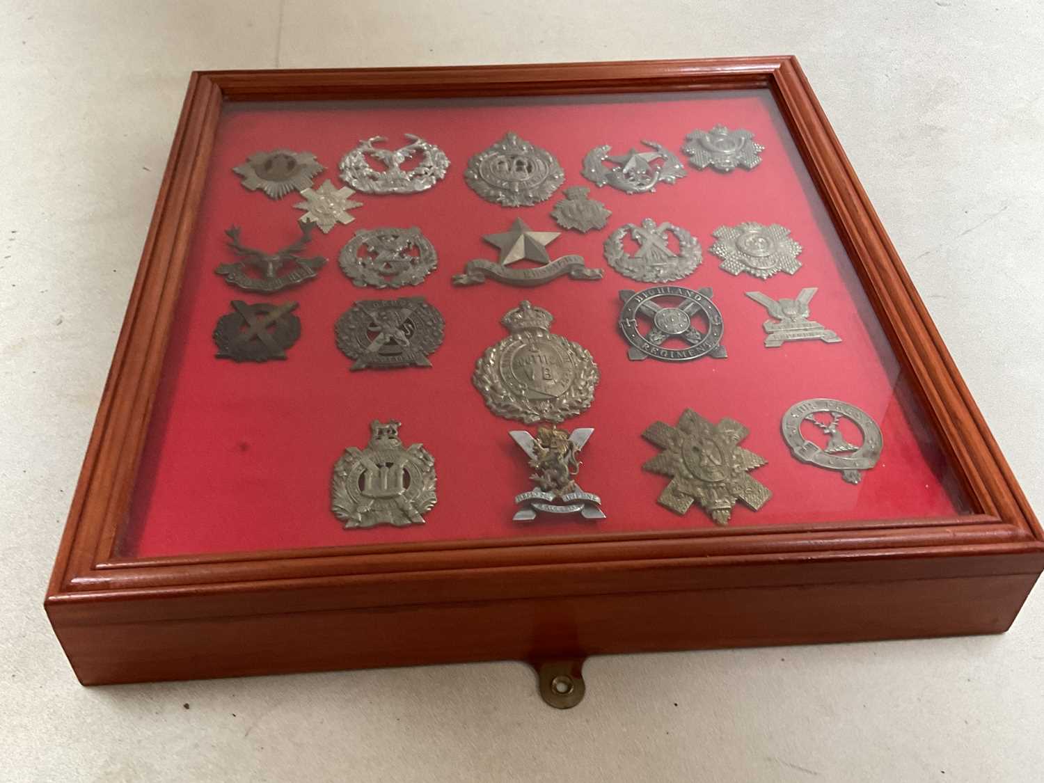 A framed and glazed display of Scottish regiment cap badges, including Highland Regiment, The