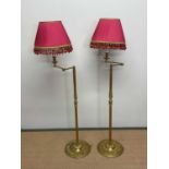 A pair of brass floor lamps with pleated shades above adjustable arms, fluted central columns and