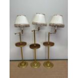 A set of three 20th century brass floor lamps with adjustable arms, fluted central columns,