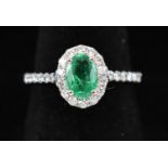 A 14ct white gold oval emerald and round brilliant cut diamond cluster ring with diamond