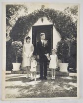 A black and white photograph of John F Kennedy and family standing before a doorway with faint