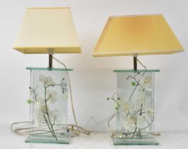 A pair of modern glass lamps containing orchids, height to top of fitment 40cm.