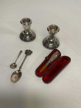 A pair of weighted silver candlesticks, a cased cigarette holder and two spoons