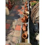 A large galvanised animal feeder, with a selection of terracotta plant pots, and a cast iron hay