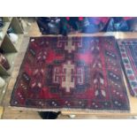 An Afghan rug with stylised decoration on a predominantly red ground.
