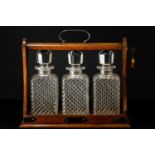 An early 20th century oak tantalus with silver plated mounts housing three ribbed glass decanters,