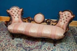 A Victorian carved walnut framed settee with scrolling back, upholstered in a salmon pink and floral