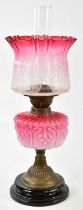 A late Victorian oil lamp, the cranberry and clear glass shade with wavy rim and frosted decoration,