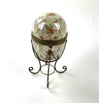 A German porcelain hand painted and 'jewelled' gilt mounted hinged egg, height including stand