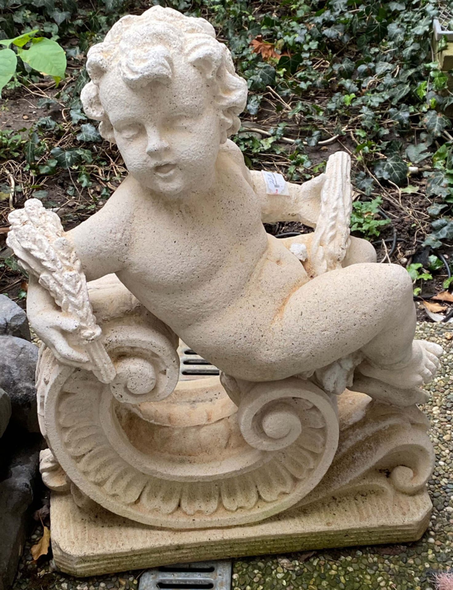 Gartenfigur als Putto mit Ähren in den Händen, auf Rocaillen sitzend. Betonguss, H=70 cm, B=54 cm,