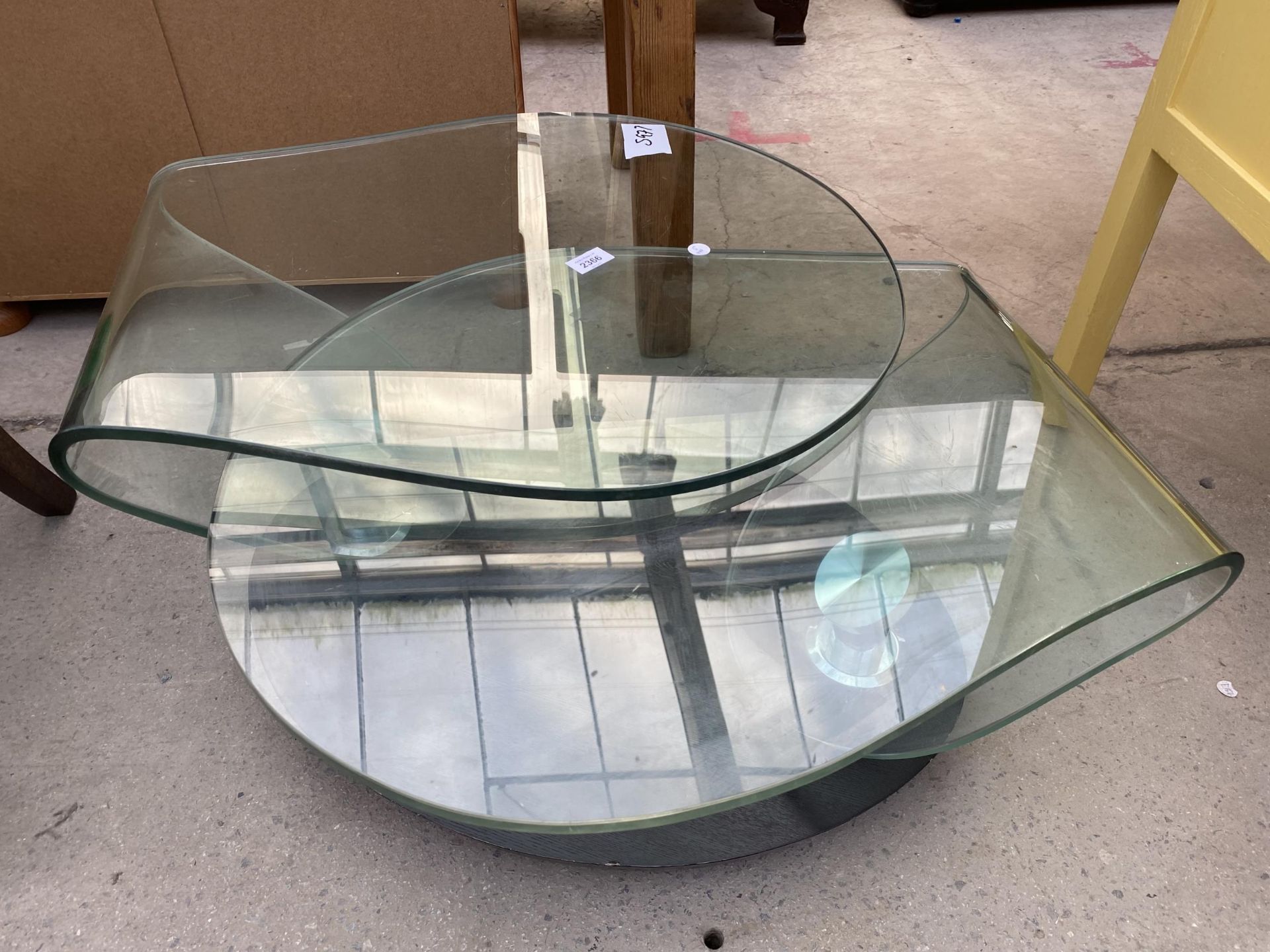 A 1970'S GLASS SWING COFFEE TABLE ON OVAL EBONISED BASE, ENCLOSING CHAIN MECHANISM