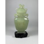 A DECORATIVE ORIENTAL JADE TYPE HARDSTONE LIDDED VASE ON WOODEN BASE, HEIGHT 19CM