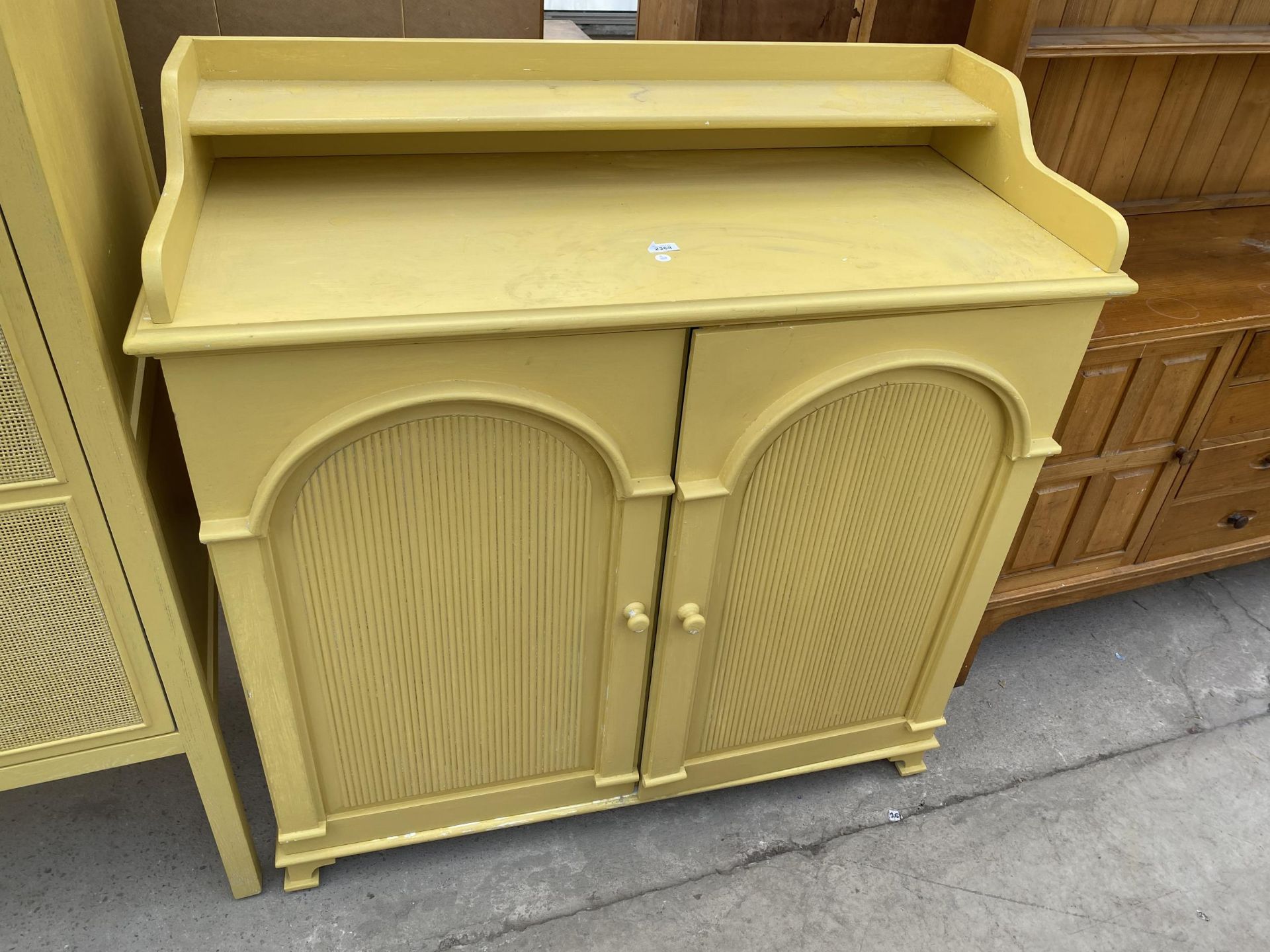 A MODERN YELLOW CUPBOARD WITH ARCHED DOORS, GALLERY BACK WITH SHELF, 45" WIDE