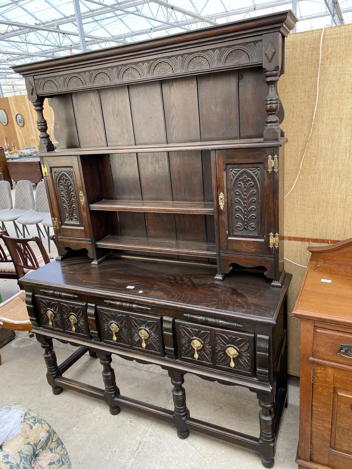 AN OAK JACOBEAN STYLE DRESSER WITH PLATE RACK ENCLOSING CUPBOARDS, THREE CARVED DRAWERS TO BASE ON