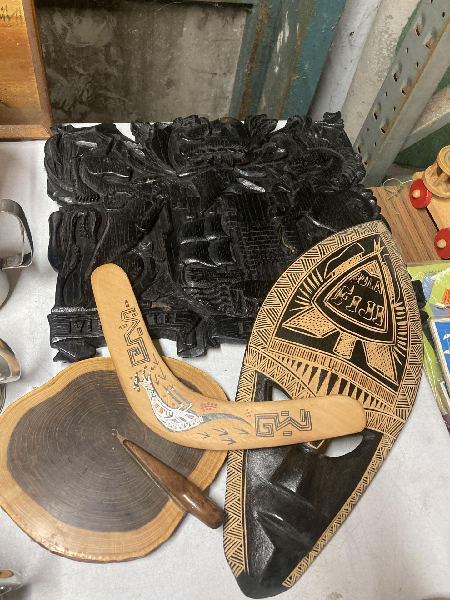 A QUANTITY OF WOODEN ITEMS TO INCLUDE A WALL PLAQUE, MASK, BOOMERANG AND CHOPPING BOARD