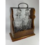 A WOODEN AND SILVER PLATED TWIN BOTTLE TANTLUS WITH TWO CUT GLASS DECANTERS, (ONE STOPPER A/F),