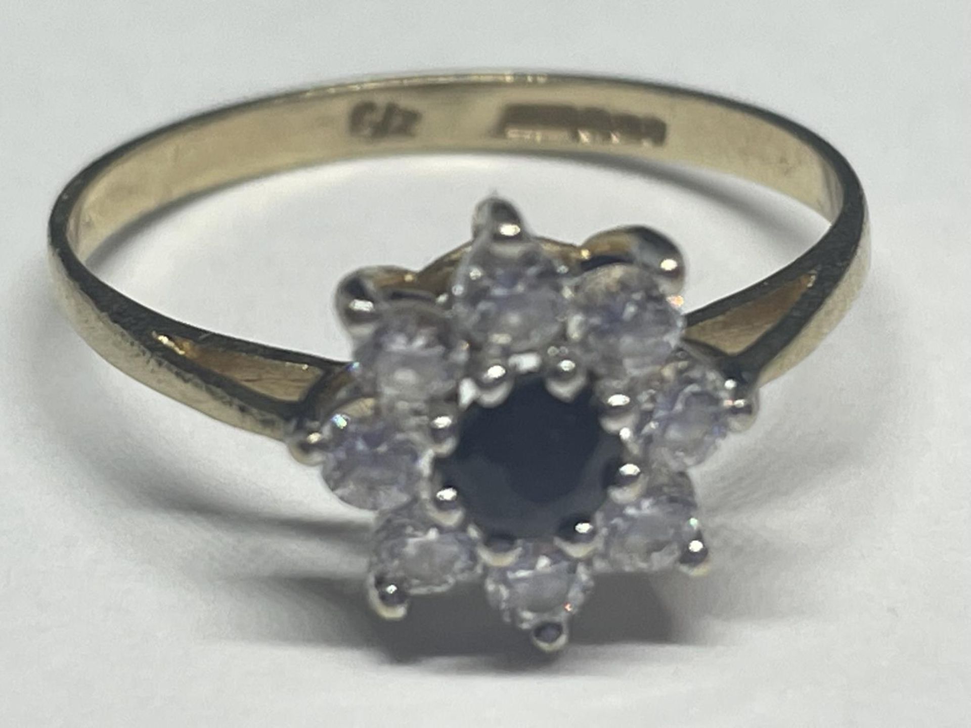 A 9 CARAT GOLD RING WITH A CENTRE SAPPHIRE SURROUNDED BY EIGHT CUBIC ZIRCONIAS IN A FLOWER DESIGN