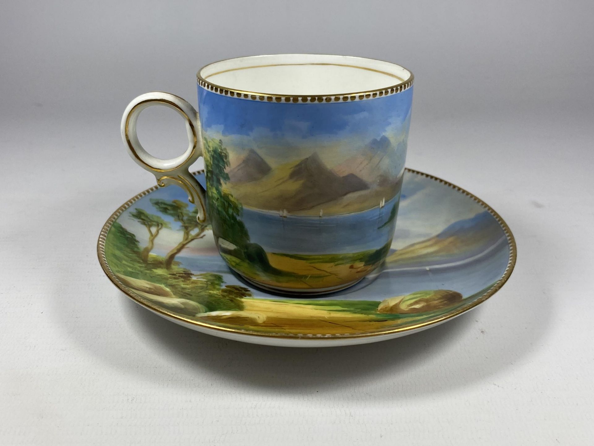 A 19TH CENTURY HAND PAINTED PORCELAIN CUP AND SAUCER WITH LAKE & CASTLE SCENE, CROSS/WING MARK TO