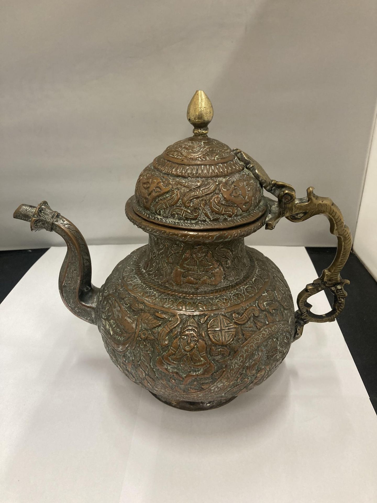 AN ASIAN STYLE COPPER TEAPOT WITH EMBOSSED DESIGN