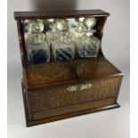 AN EDWARDIAN INLAID OAK THREE BOTTLE TANTALUS HOLDER WITH TWIN LIDDED COMPARTMENT AND LOWER DRAWER