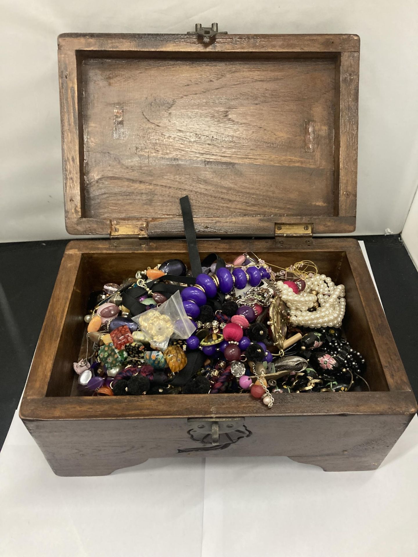 A VINTAGE MAHOGANY BOX CONTAINING A QUANTOITY OF COSTUME JEWELLERY TO INCLUDE NECKLACES,