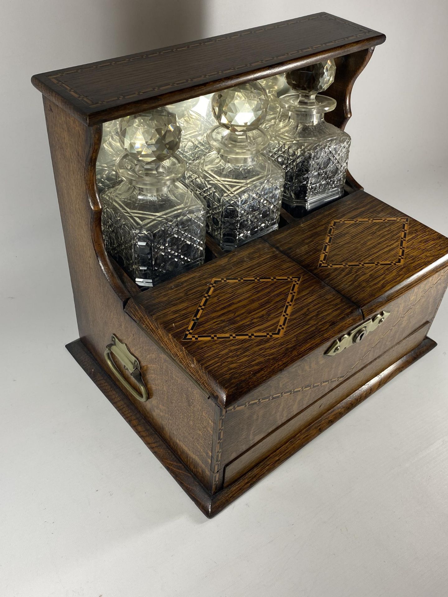 AN EDWARDIAN INLAID OAK THREE BOTTLE TANTALUS HOLDER WITH TWIN LIDDED COMPARTMENT AND LOWER DRAWER - Image 2 of 6