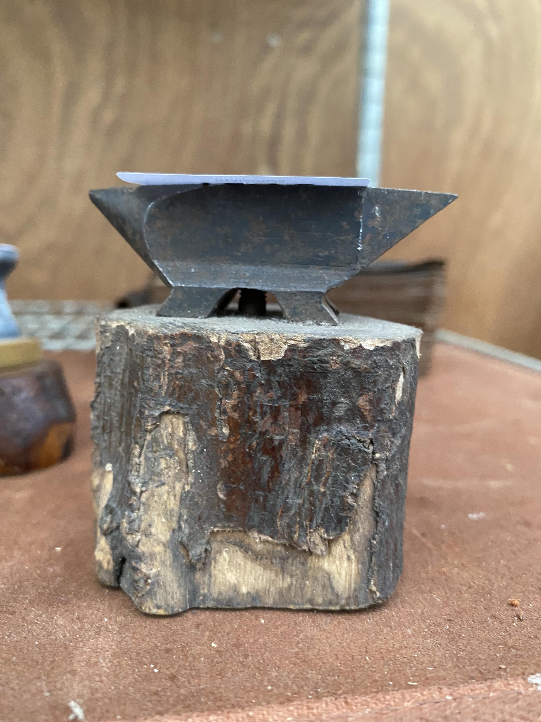 A MINITURE SAMPLE ANVIL ON A LOG BASE